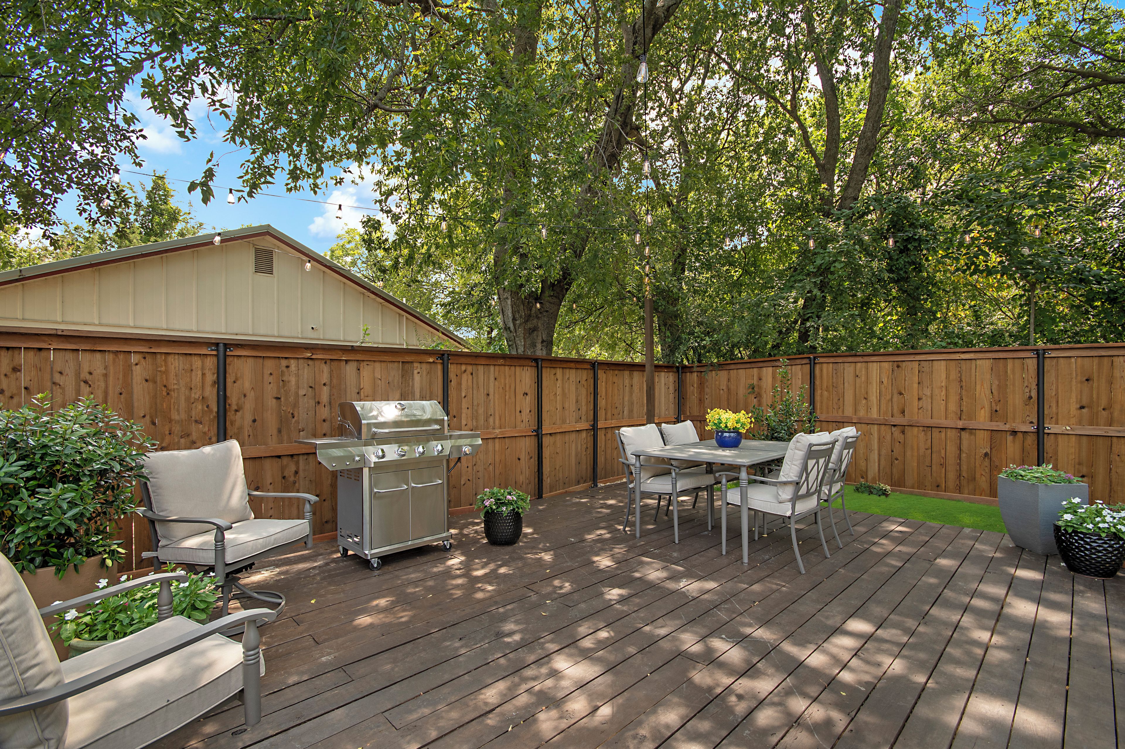 A wooden deck with a grill, outdoor furniture, and potted plants.