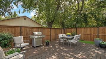 A wooden deck with a grill, outdoor furniture, and potted plants.