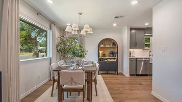 A dining area with a table set for four, a chandelier, and a view of the outdoors through a window.