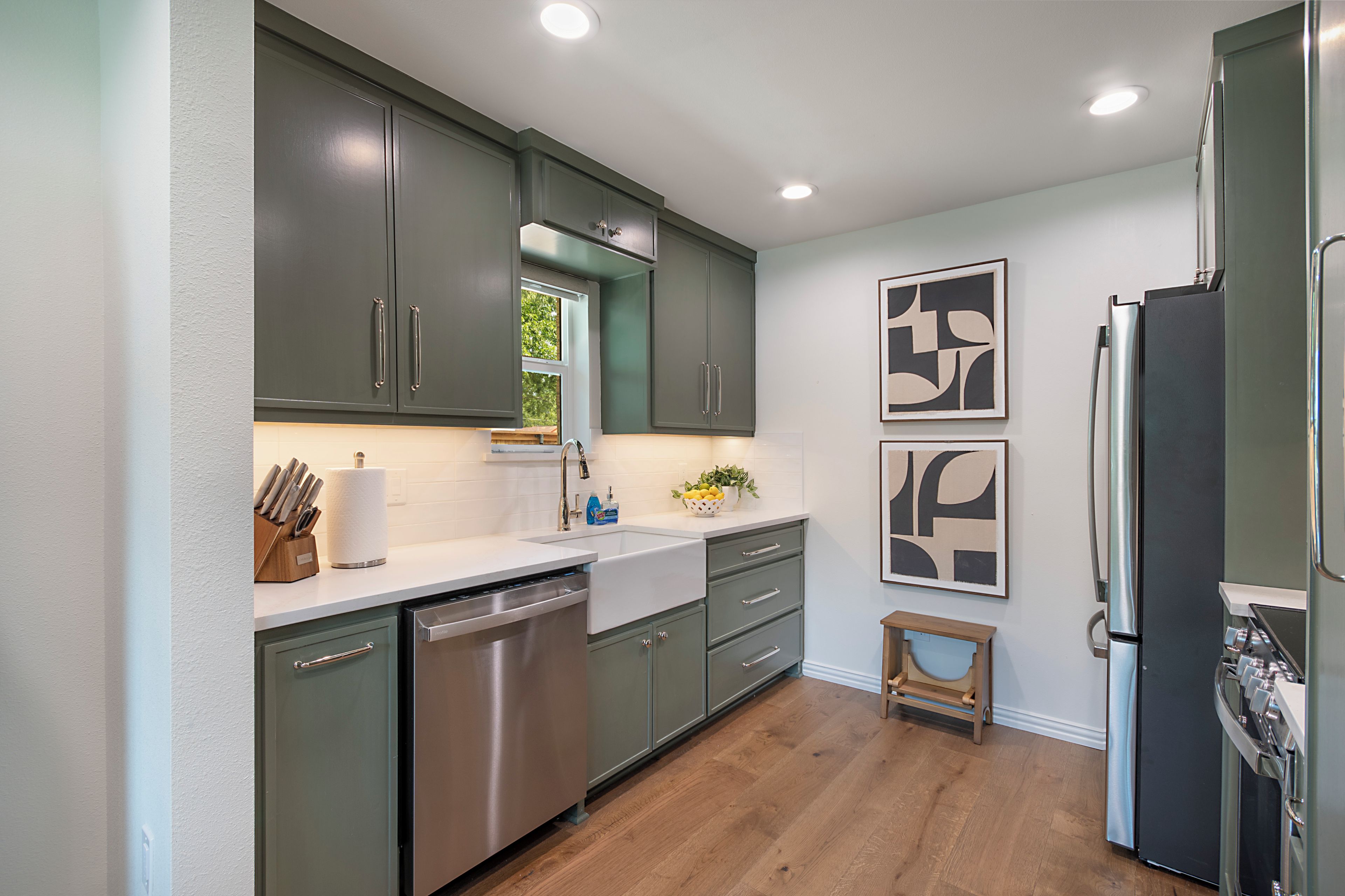 A modern kitchen with stainless steel appliances, green cabinets, and a wooden floor.