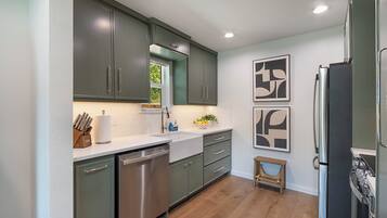 A modern kitchen with stainless steel appliances, green cabinets, and a wooden floor.