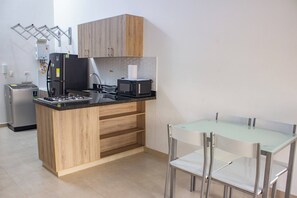 Una cuina compacta amb fornet integrat, microones i una petita zona de dinar amb taula de vidre i cadires metàl·liques.