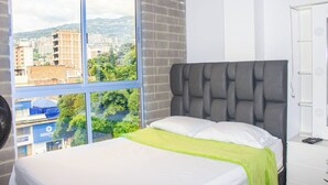 A bedroom with a large window, a bed with white and green bedding, and a grey upholstered headboard. - 51 Close to Laureles, Metro and Restaurants (Medellín)