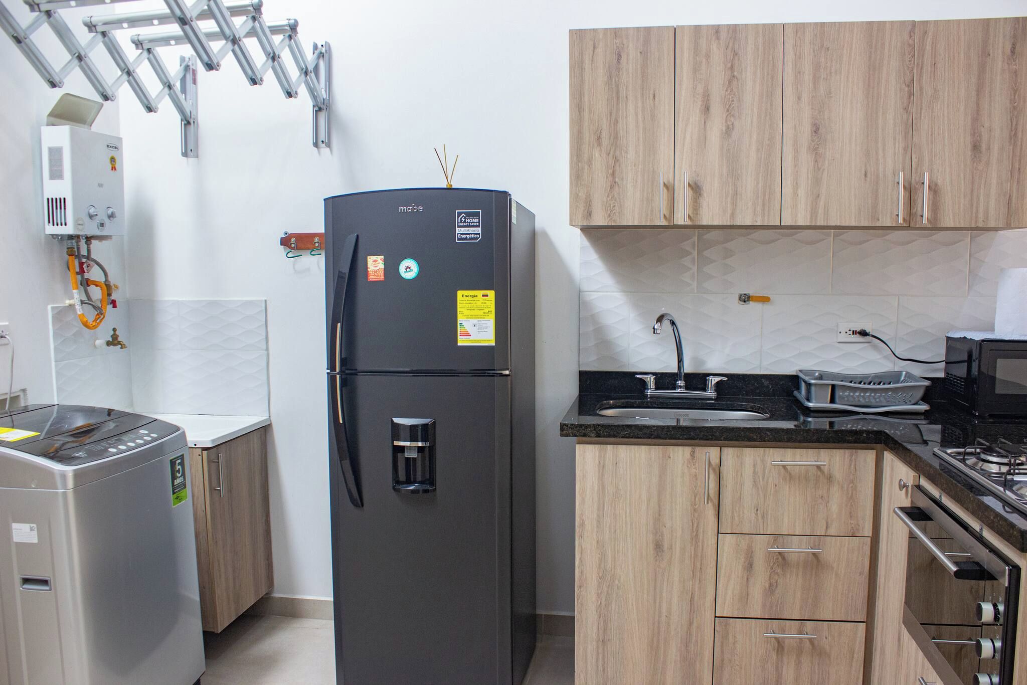 Una cocina moderna con un refrigerador negro, armarios de madera, un lavamanos de acero inoxidable y un microondas.