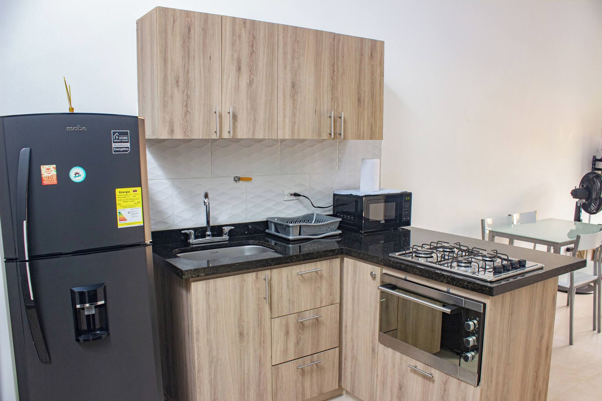 Cocina compacta equipada con refrigerador, microondas, estufa y pileta.