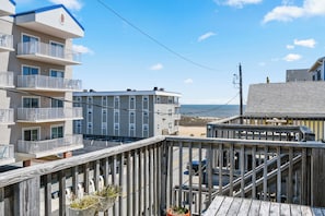 Ein mehrstöckiges Gebäude mit Balkonen, einer Holzterrasse und Blick auf den Strand.
