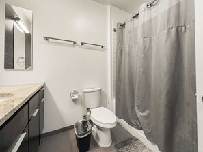 Een badkamer met toilet, wastafel, spiegel, douchegordijn en prullenbak.