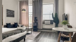 A modern hotel room with a bed, a desk, a chair, a potted plant, and a large window with curtains. - Compact Studio for a Relaxed Stay (Chicago)