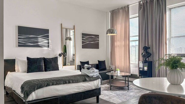 A modern hotel room with a large bed, a desk, and a view of the city through large windows. - Compact Studio for a Relaxed Stay (Chicago)