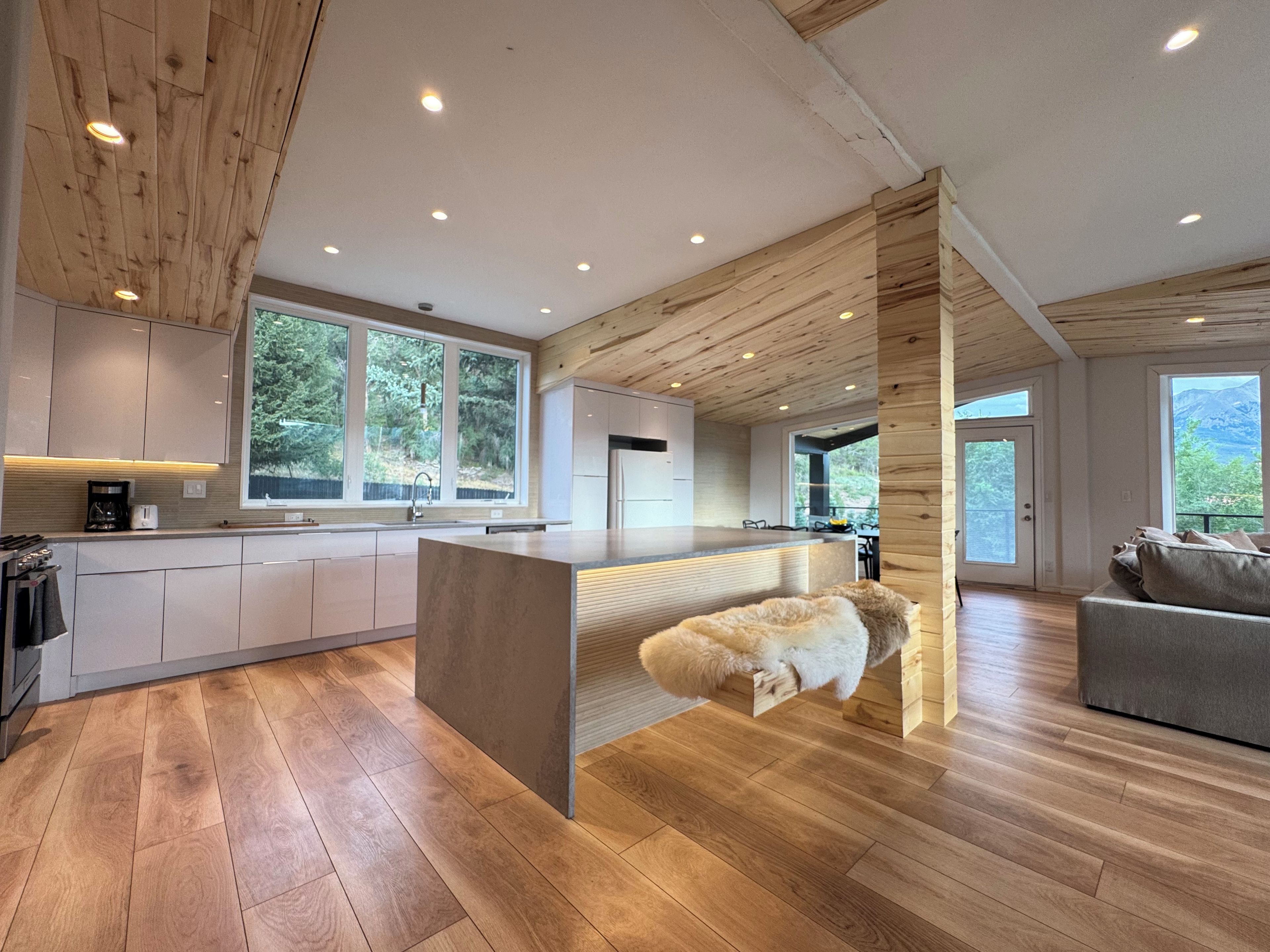 Una cocina moderna con vigas de madera en el techo, una isla central y amplios ventanales con vistas al exterior.
