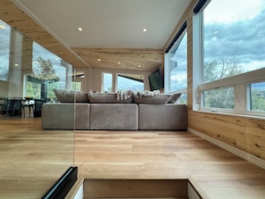 A modern interior with a sectional sofa, large windows, and a dining area. - Sopris Mountain Retreat w/ Pool & Mountain Views (Carbondale)