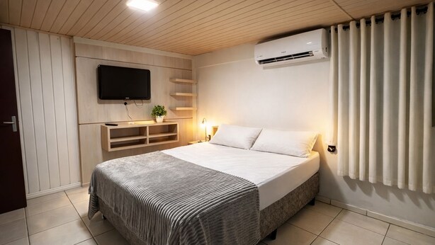 Un dormitorio con cama, televisión montada en la pared, estantería empotrada y aire acondicionado.