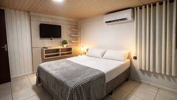 A bedroom with a bed, a television mounted on the wall, a built-in shelf, and an air conditioning unit.