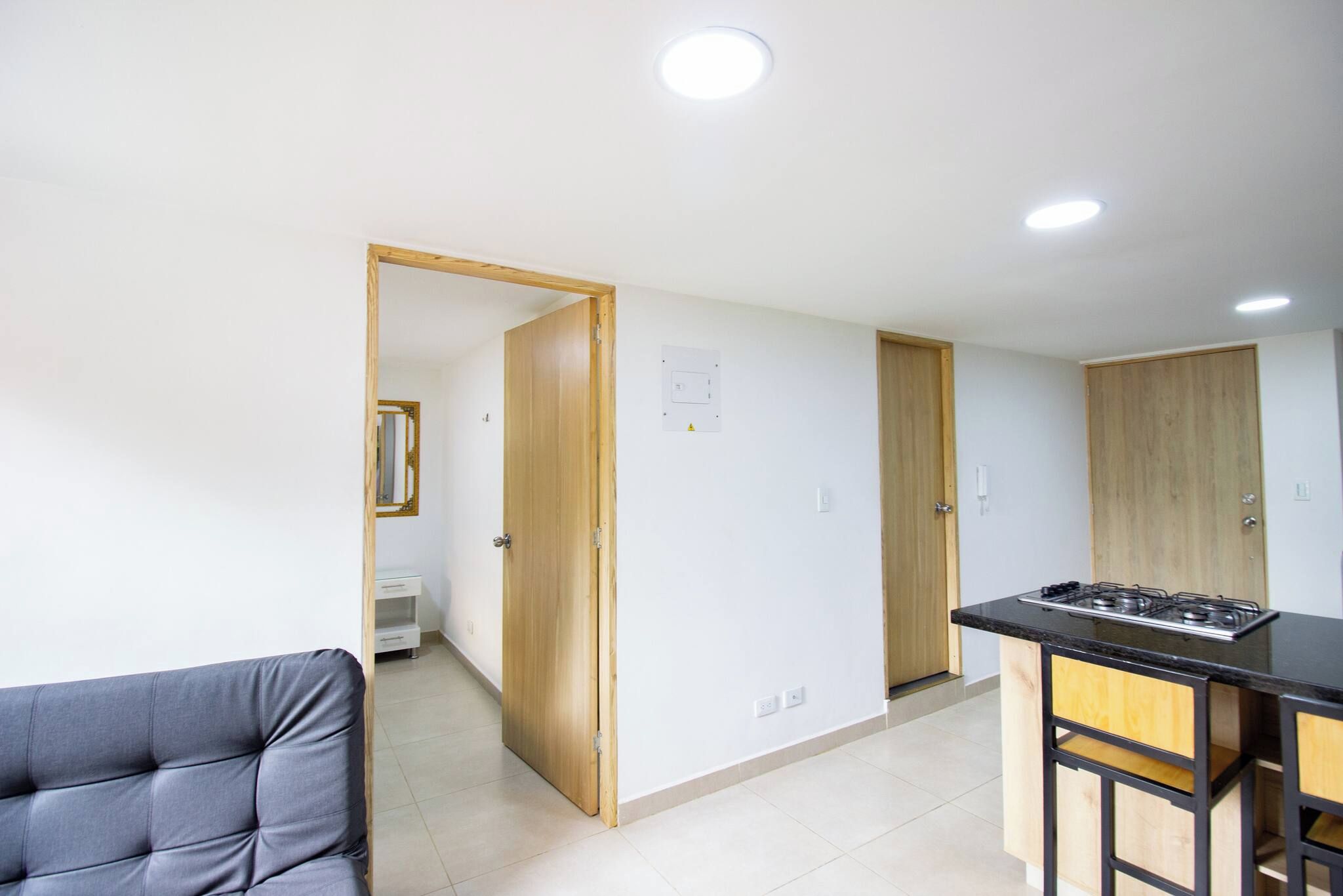 Una cocina moderna con encimera negra y armarios de madera, un sofá gris y una puerta de madera que da a otra habitación.