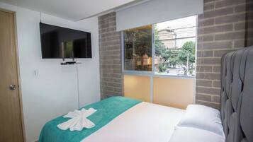Habitación de hotel con cama, televisión montada en la pared, ventana con vista a la calle y una puerta.