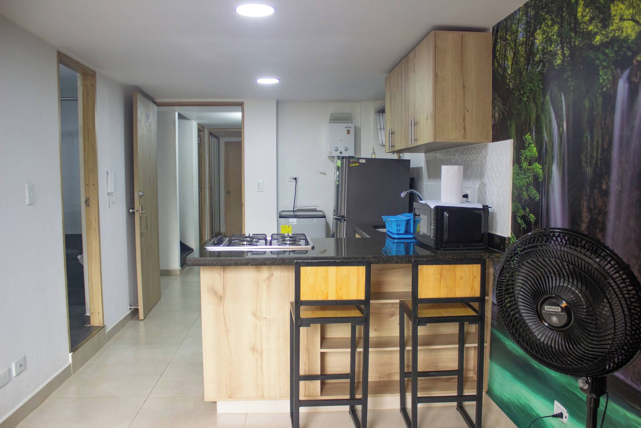 Una cocina con una isla central, taburetes de bar, un refrigerador, un microondas y un ventilador.