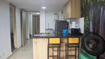 Una cocina con una isla central, taburetes de bar, un refrigerador, un microondas y un ventilador.