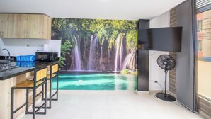 Cozinha com mural de cachoeira, micro-ondas e ventilador.