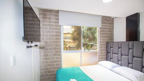 Quarto de hotel com cama, janela com vista, televisão na parede e parede de tijolos.