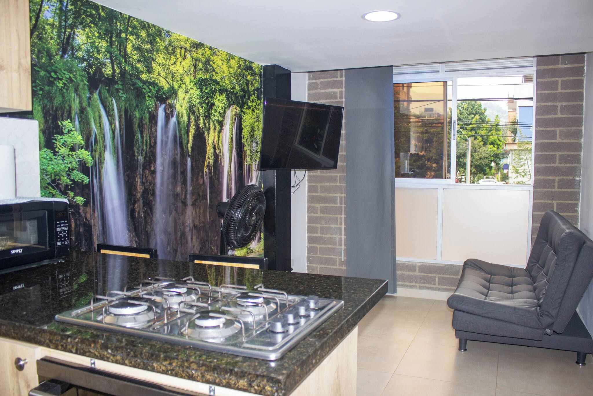 A modern kitchen with a gas stove, a microwave, and a large waterfall mural on the wall.