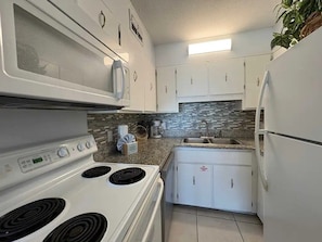 A compact kitchen with white cabinets, a microwave, a stove, and a sink. - The Summit 325 (Panama City Beach)
