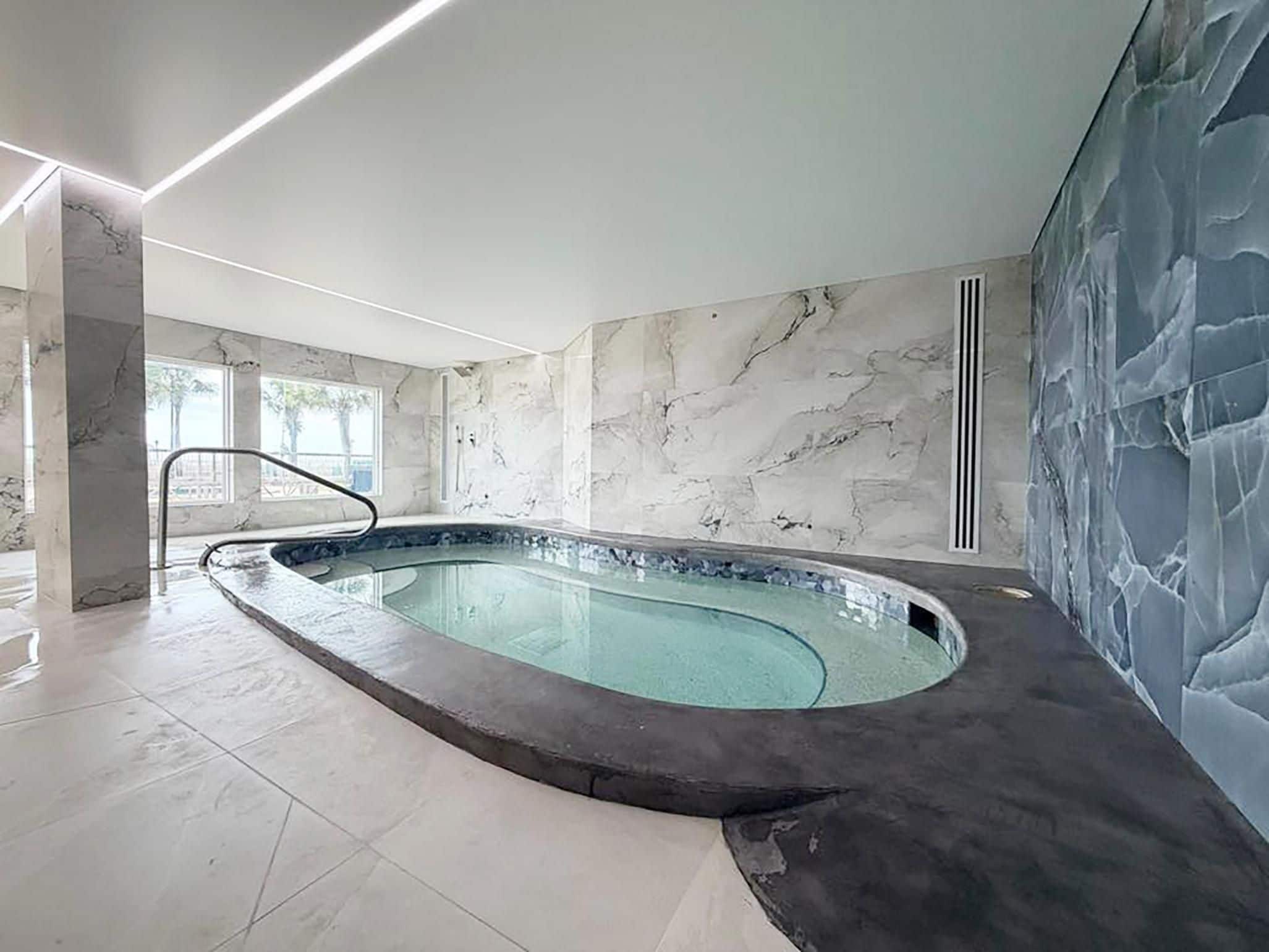 Una piscina interior moderna con pared y techo de mármol, una barrera de cristal transparente y suelo de baldosas.
