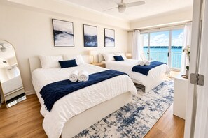 A hotel room with two beds, a large window with a view of the sea, and a ceiling fan. - 3BR Bayfront | Boardwalk |Sunsets Balcony |Pool | Parking (Ocean City)