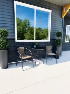 A patio with two chairs and a table, a large window, and potted plants.