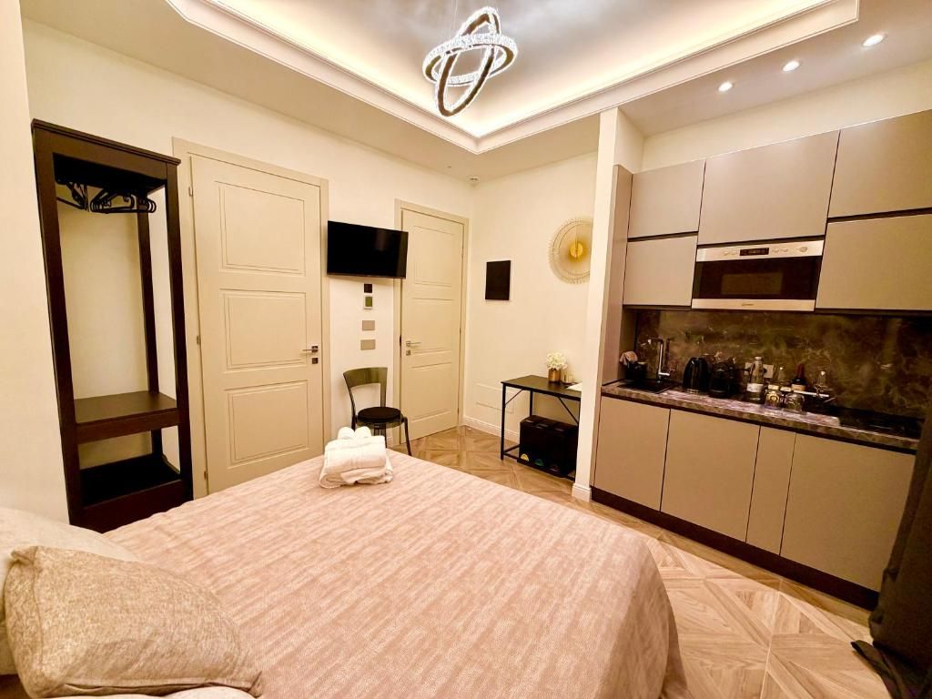 A hotel room with a bed, a television, a kitchenette, and a door leading to a hallway.