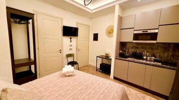 A hotel room with a bed, a television, a kitchenette, and a door leading to a hallway.