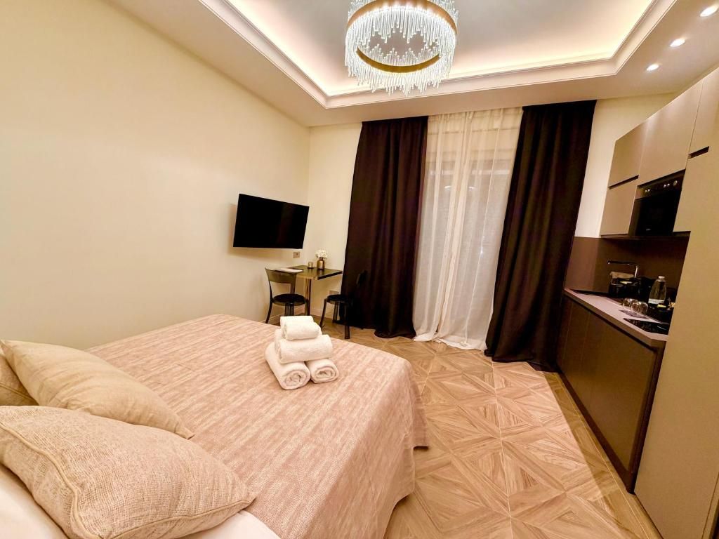 A hotel room with a bed, a TV, a desk, and a kitchenette.