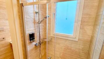 Une douche fermée par des parois en verre, dotée d’un pommeau de douche à main et d’un autre pommeau de douche à main fixé au mur.