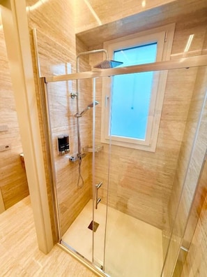 A glass-enclosed shower with a handheld showerhead and a handheld shower head on the wall.