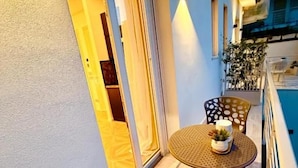 Un balcón con una mesa y sillas, una planta en maceta y un ventanal corredizo que da a un espacio interior.