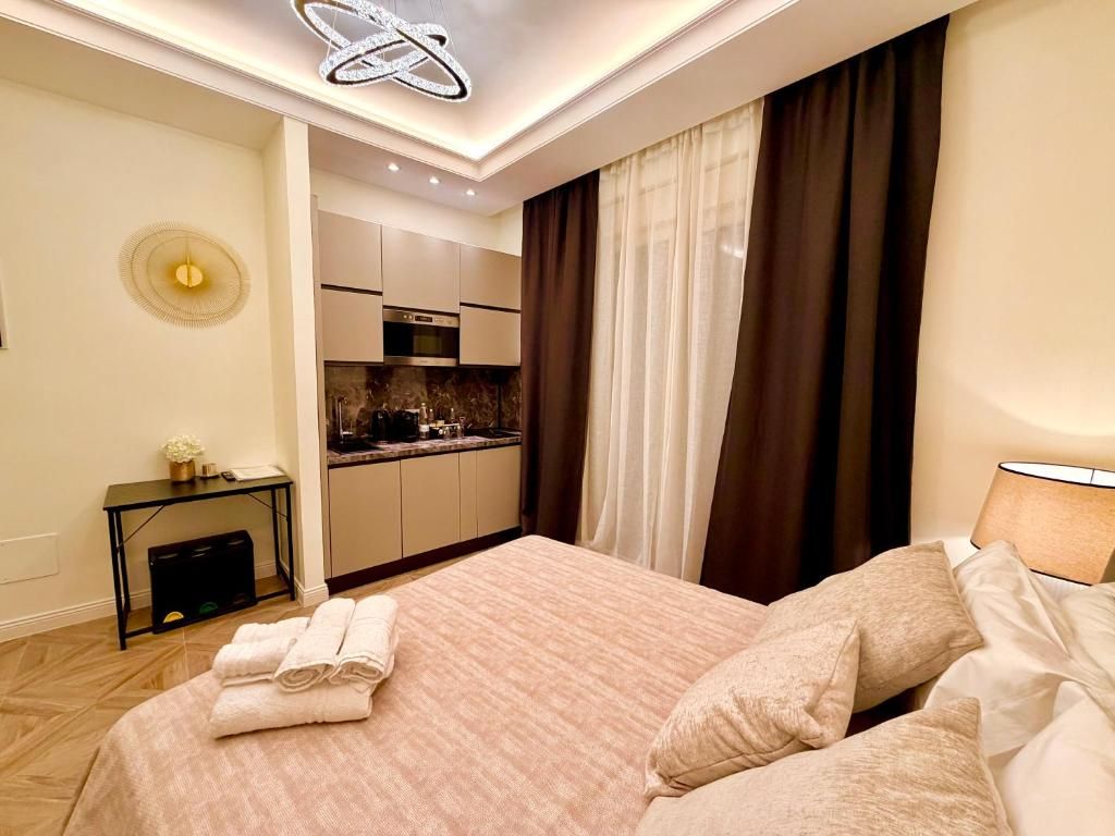 Ein Hotelzimmer mit einem Bett, einem Nachttisch, einer Lampe, Blick auf die Küche und einer Deckenleuchte.