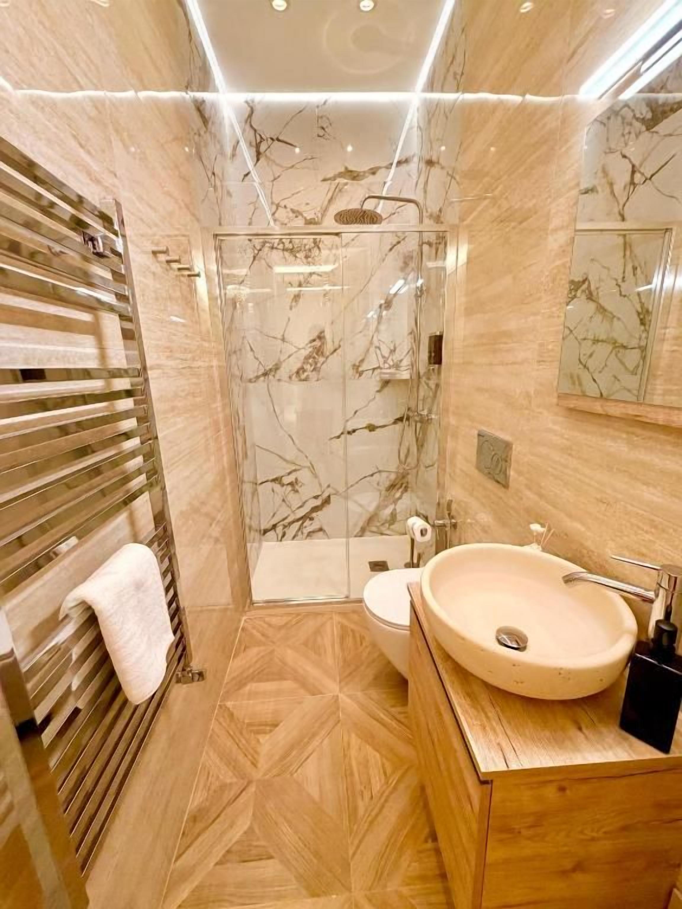 Un baño con piso de mármol, cabina de ducha de vidrio, lavamanos y un inodoro.