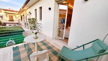 Un balcon avec un tapis à carreaux, une table avec des chaises et un fauteuil de jardin vert.