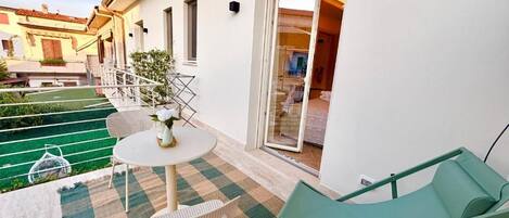 Un balcón con un tapete a cuadros, una mesa con sillas y una sillona verde.
