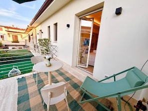 A balcony with a checkered mat, a table with chairs, and a green lounge chair.