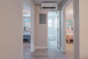 Un pasillo con una unidad de aire acondicionado en el techo, que conduce a un dormitorio con una cama y un ventanal.
