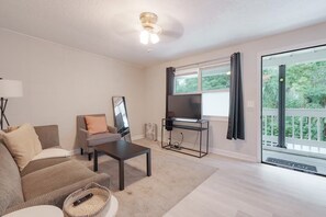 A living room with a sofa, a coffee table, a TV on a stand, a floor lamp, and a window with curtains. - Mins 2 Everbank - Baptist UF - Health - Beach - Airport (Jacksonville)
