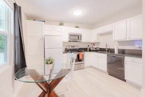 Una cocina moderna con gabinetes blancos, electrodomésticos de acero inoxidable y una mesa de comedor de vidrio.