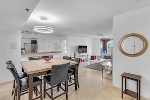 A modern dining area with a wooden table and black chairs, a kitchen with a refrigerator and cabinets, and a living area with a sofa and a TV. - Aventura Palm Retreat - 2BR Pool Gym Tennis (Aventura)