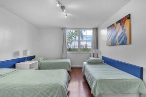 Ein Hotelzimmer mit zwei Einzelbetten, einem Fenster mit Blick auf Gebäude, einem Bild an der Wand und einer Deckenleuchte.
