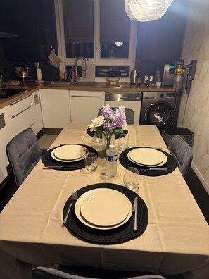 Una mesa de comedor dispuesta con platos, cubiertos y un florero en una cocina moderna con lavadora y armarios.