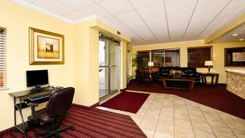 A hotel lobby with a desk, computer, office chair, sofa, and a red carpet.