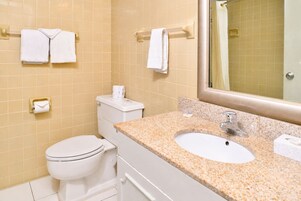 Un baño con inodoro, lavamanos y espejo. Hay toallas colgadas en los porta-toallas.