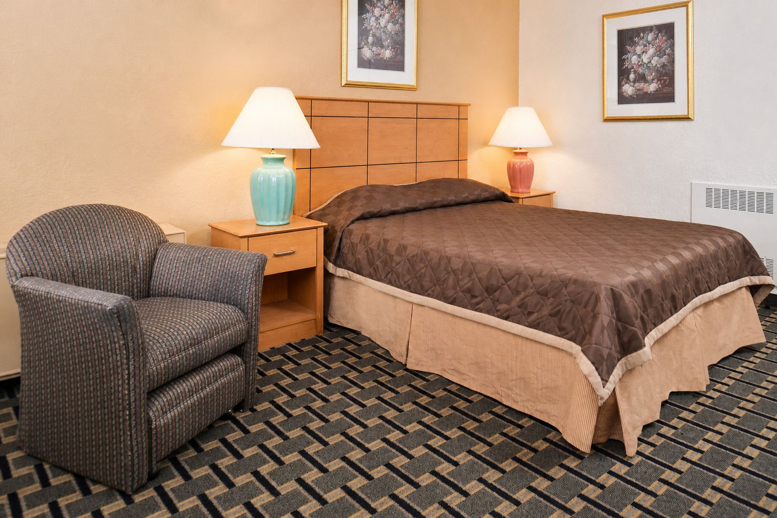 A hotel room with a bed, a chair, two bedside tables with lamps, and a patterned carpet.