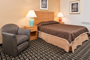A hotel room with a bed, a chair, two bedside tables with lamps, and a patterned carpet.