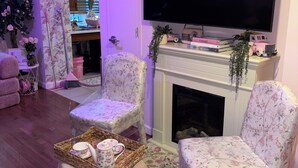 Ein Wohnzimmer mit Kamin, zwei floral gepolsterte Sessel, einem Fernseher und einem Tablett mit Dekoration.